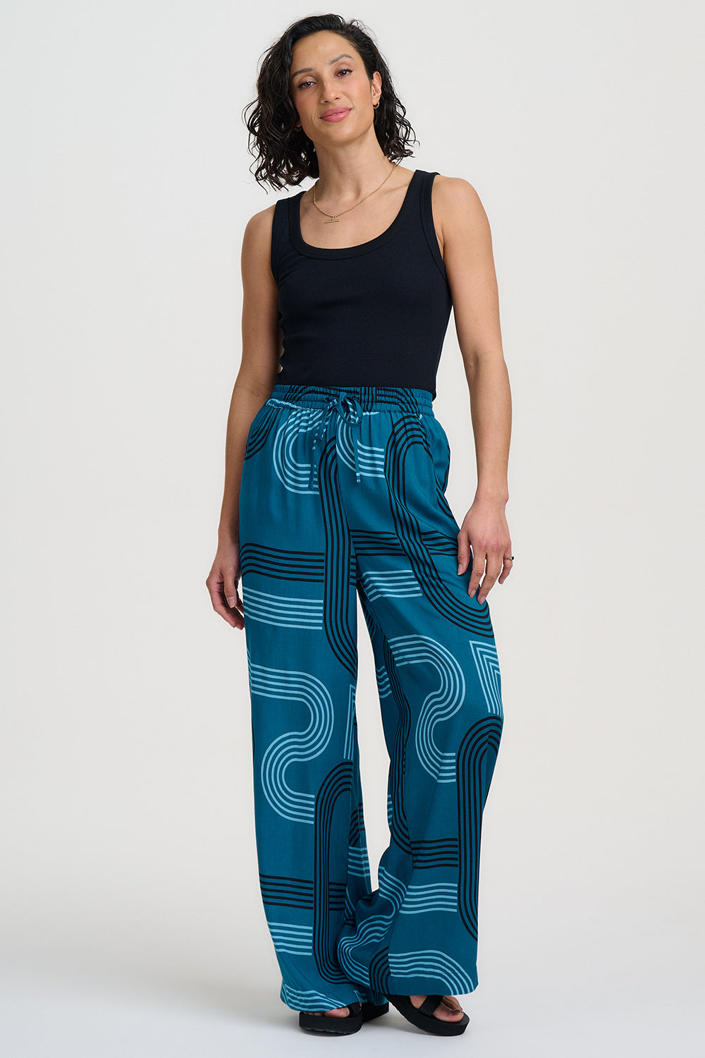 Woman wearing blue patterned pants and a black top on a white background