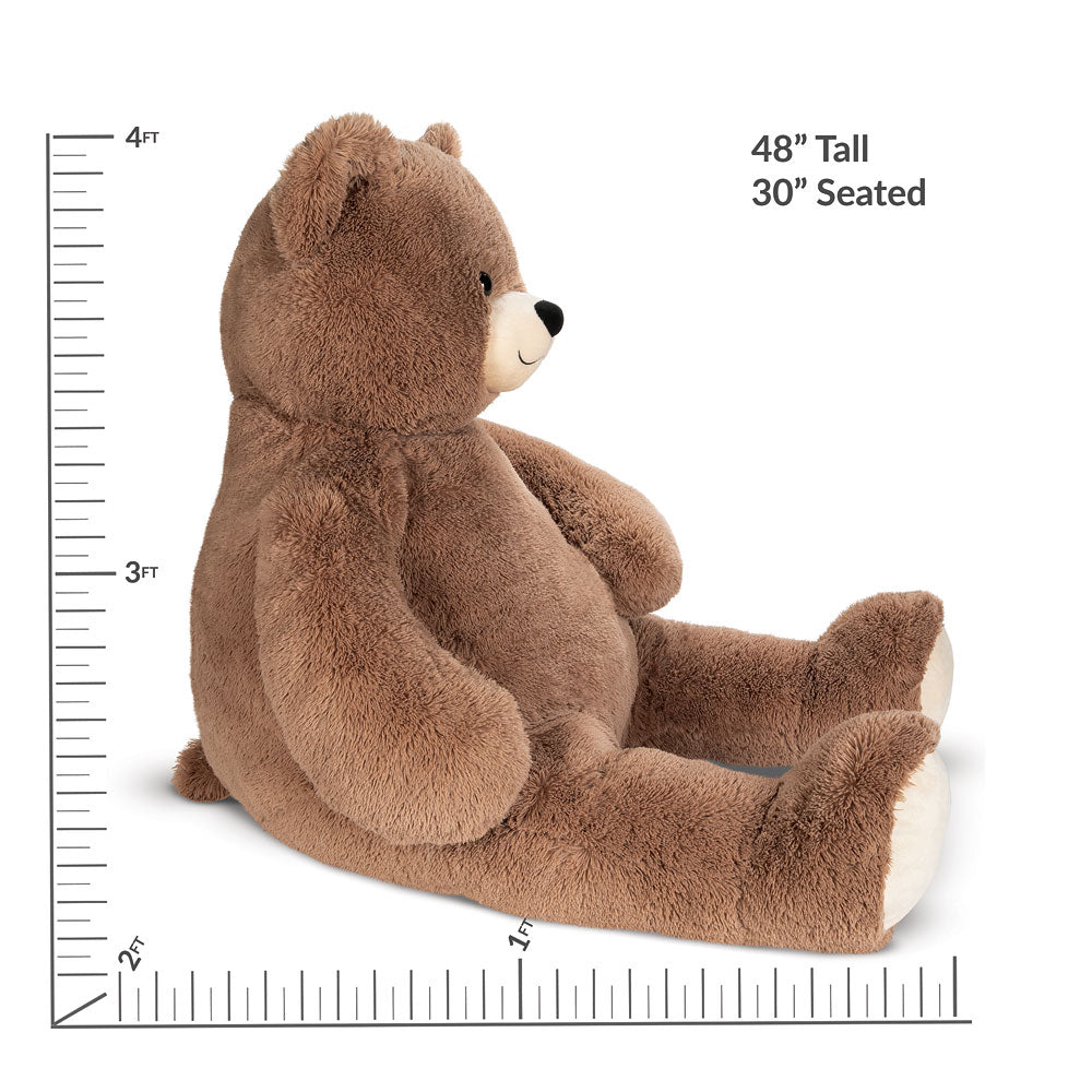 Brown plush teddy bear sitting with white snout and paw pads, about 4 feet tall.